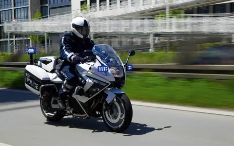 Policyjny motocykl BMW F800GT z włączonymi sygnałami świetlnymi pędzi po drodze.