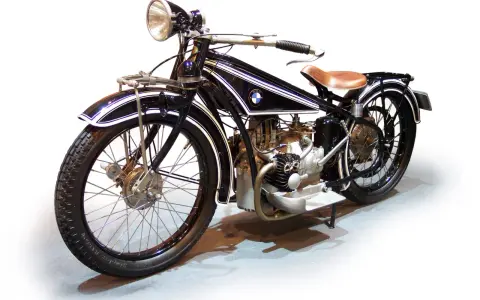 Klasyczny motocykl BMW z lat 20. XX wieku, czarny z białymi pasami, z brązowym siodłem. Ikona historii BMW.