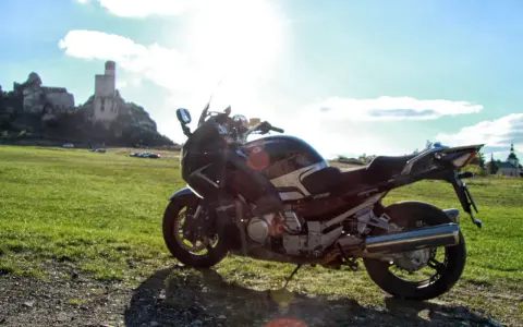 Motocykl na tle zamku na skale i zielonej łąki.
