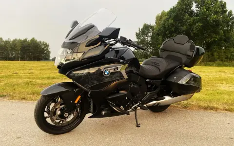 Czarny motocykl BMW K1600 Grand America z kuframi, gotowy na daleką podróż pośród zielonych pól i drzew.