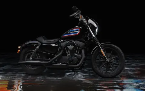 Czarny Harley-Davidson Iron 1200 z kolorowym paskiem na baku, stojący na mokrej, błyszczącej nawierzchni.