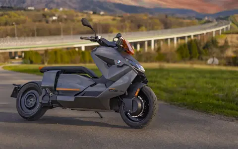 Szary skuter elektryczny BMW CE 04 na tle malowniczego krajobrazu z mostem i wzgórzami.