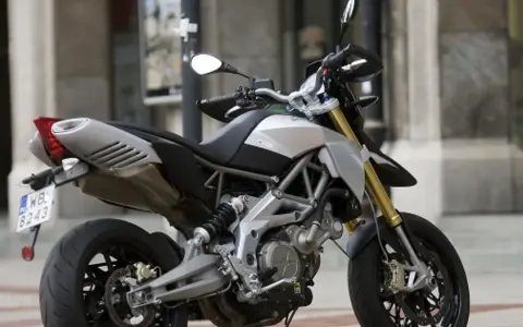 Srebrno-czarny motocykl Aprilia Dorsoduro 750 z żółtymi lagami, gotowy do jazdy po miejskich ulicach.