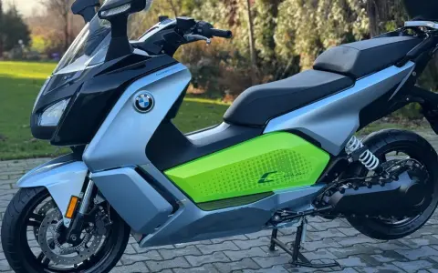 Srebrno-czarny skuter elektryczny BMW C Evolution z zielonym akcentem i napisem "C Evolution" na boku, stojący na chodniku.