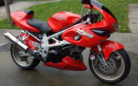 Czerwony motocykl Suzuki TL1000 z napisem "V-TWIN SUPER SPORT" na owiewce, zaparkowany na mokrej nawierzchni obok trawnika.