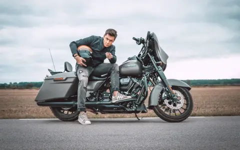 Mężczyzna w czarnej kurtce i podartych jeansach siedzi na motocyklu Harley-Davidson Street Glide, trzymając kask.