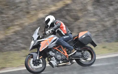 Motocyklista w kasku i kombinezonie śmiga na KTM Super Duke 1290 GT w deszczu.