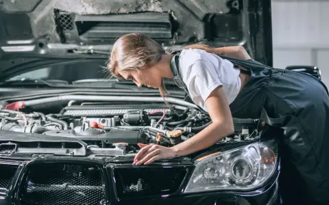 Młoda mechaniczka pochyla się nad silnikiem, sprawdzając go. To może być początek jej drogi, jak otworzyć warsztat samochodowy.