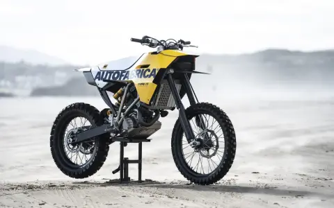 Żółto-biały motocykl customowy Autofabrica Type 17, bazujący na BMW G450X, stoi na plaży.