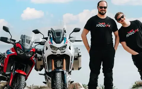 Dwóch mężczyzn w koszulkach 1000PS obok motocykli Honda Africa Twin.