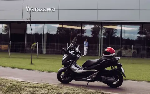 Elegancki skuter Honda Forza 300 zaparkowany przed budynkiem z napisem "Warszawa". Czerwony kask leży na siedzeniu.