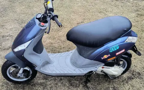 Niebieski skuter z naklejkami Red Bull i Motul na tle trawy.