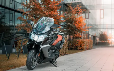 Skuter BMW C650 GT z brązowym siedzeniem na tle nowoczesnego budynku i jesiennych drzew. Dane techniczne tego modelu są imponujące.
