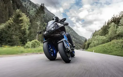 Motocyklista na Yamaha Niken pokonuje górską drogę, otoczony zielonymi lasami i skalistymi szczytami.