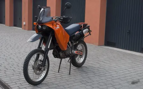 Pomarańczowy motocykl KTM 640 Adventure stoi na brukowanym podjeździe przed garażami.