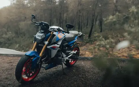 Niebiesko-biały motocykl BMW F900R z czerwonymi felgami na tle jesiennego lasu.