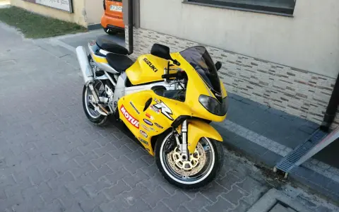Żółty motocykl Suzuki TL1000R z naklejkami sponsorów, zaparkowany na chodniku.