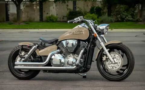 Beżowy motocykl Honda VTX 1300 z chromowanymi elementami i czarnym siedzeniem, zaparkowany na ulicy.