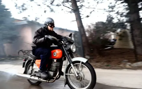 Mężczyzna w kasku i goglach pędzi na pomarańczowym motocyklu WSK 125. Widać dym z rury wydechowej, sugerujący dużą prędkość maksymalną.
