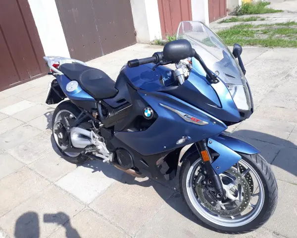 Błękitny motocykl BMW F800 GT stoi na chodniku przed garażem.