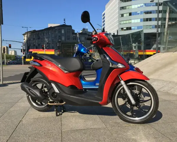 Czerwony Piaggio Liberty 125, obok niebieskiego, na tle miasta. Idealny do sprawdzenia piaggio liberty 125 dane techniczne.