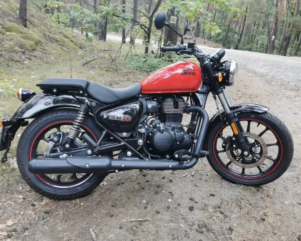 Czerwony Royal Enfield Meteor 350 na leśnej drodze. Klasyczny wygląd i nowoczesna technologia w jednym.