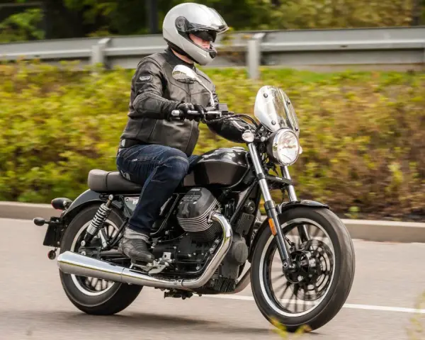 Motocyklista w kasku i skórzanej kurtce jedzie na stylowym motocyklu Moto Guzzi V9.