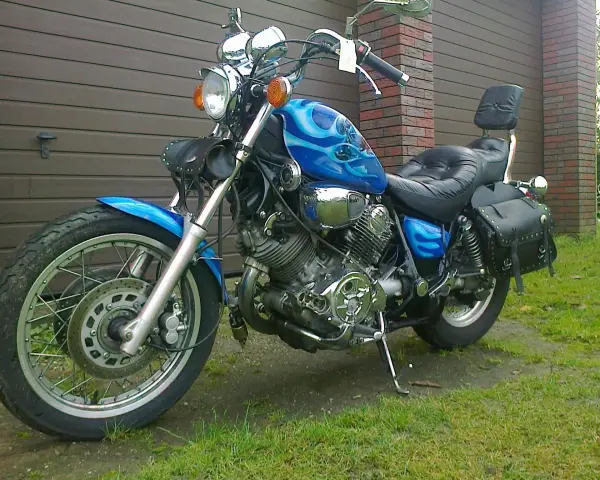 Błękitny motocykl Yamaha Virago 1100 z płomieniami, skórzanymi sakwami i oparciem. Wady i zalety tego klasyka do rozważenia przed zakupem.