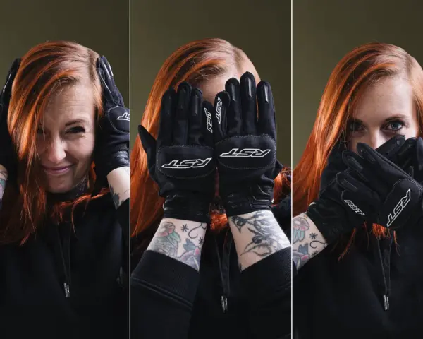 Kobieta z rudymi włosami w czarnych rękawicach motocyklowych zakrywa twarz.