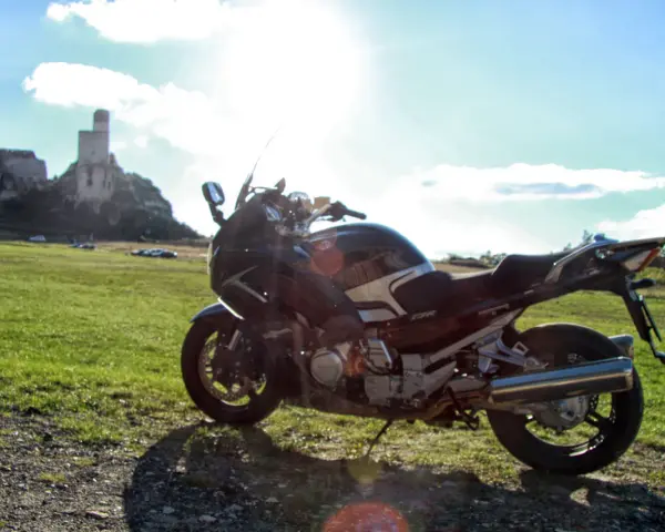 Motocykl na tle zamku na skale i zielonej łąki.