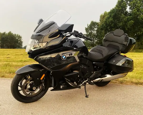 Czarny motocykl BMW K1600 Grand America z kuframi, gotowy na daleką podróż pośród zielonych pól i drzew.