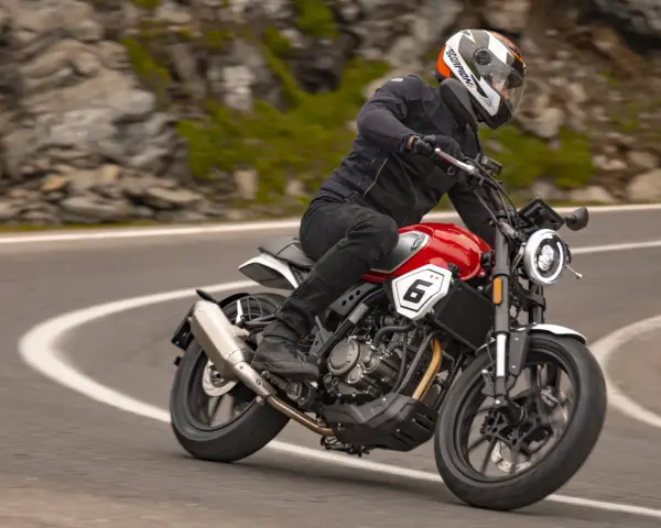 Motocyklista w kasku jedzie czerwonym motocyklem po krętej drodze. Idealny motor na początek przygody z jazdą.