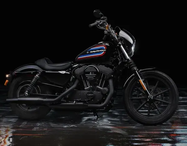 Czarny Harley-Davidson Iron 1200 z kolorowym paskiem na baku, stojący na mokrej, błyszczącej nawierzchni.