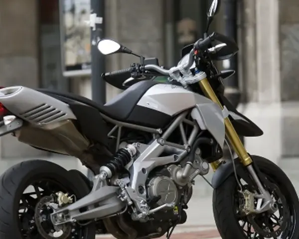 Srebrno-czarny motocykl Aprilia Dorsoduro 750 z żółtymi lagami, gotowy do jazdy po miejskich ulicach.