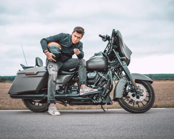 Mężczyzna w czarnej kurtce i podartych jeansach siedzi na motocyklu Harley-Davidson Street Glide, trzymając kask.