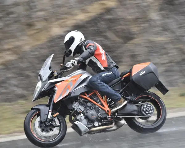 Motocyklista w kasku i kombinezonie śmiga na KTM Super Duke 1290 GT w deszczu.