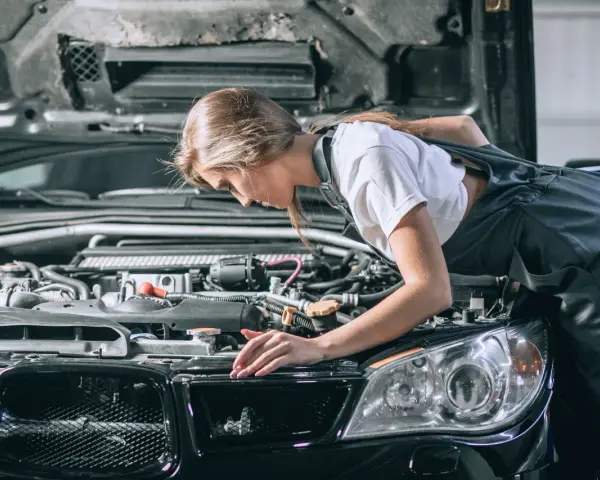 Młoda mechaniczka pochyla się nad silnikiem, sprawdzając go. To może być początek jej drogi, jak otworzyć warsztat samochodowy.