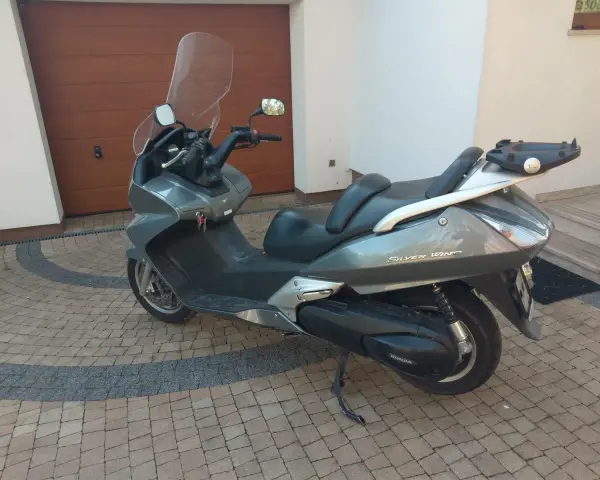 Szary skuter Honda Silver Wing 600 stoi na kostce brukowej przed garażem.