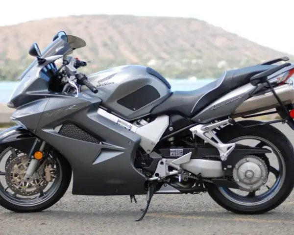 Szary motocykl Honda VFR 800 z widokiem na wodę i wzgórza w tle.