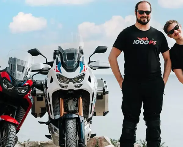 Dwóch mężczyzn w koszulkach 1000PS obok motocykli Honda Africa Twin.