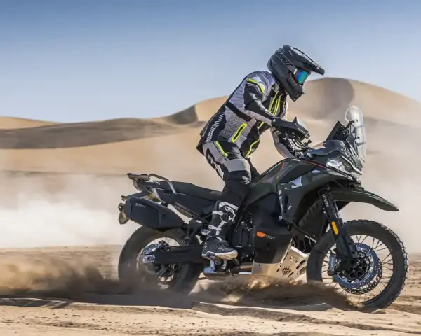 Motocyklista w pełnym rynsztunku szaleje na pustyni na swoim KTM 790 Adventure, wzbijając tumany piasku.