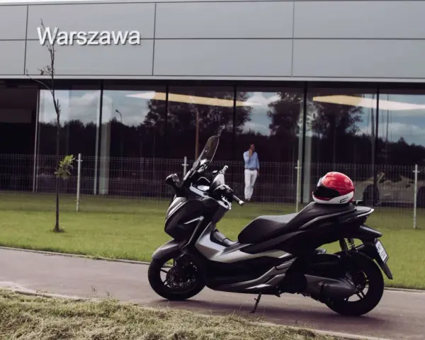 Elegancki skuter Honda Forza 300 zaparkowany przed budynkiem z napisem "Warszawa". Czerwony kask leży na siedzeniu.
