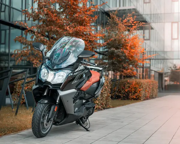 Skuter BMW C650 GT z brązowym siedzeniem na tle nowoczesnego budynku i jesiennych drzew. Dane techniczne tego modelu są imponujące.