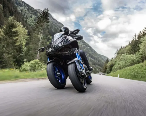Motocyklista na Yamaha Niken pokonuje górską drogę, otoczony zielonymi lasami i skalistymi szczytami.