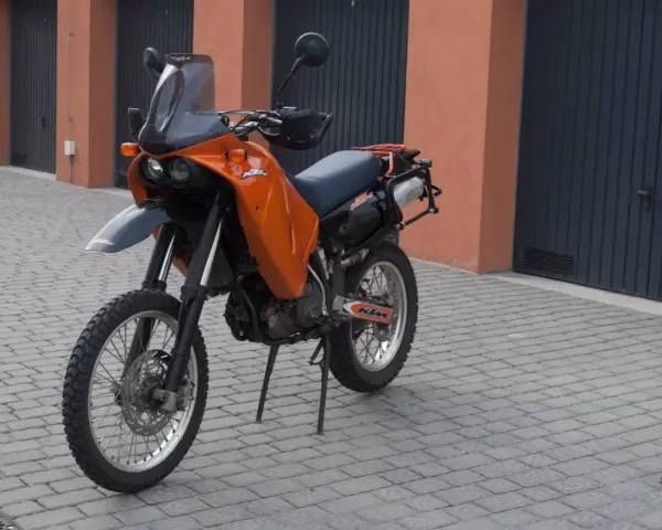 Pomarańczowy motocykl KTM 640 Adventure stoi na brukowanym podjeździe przed garażami.