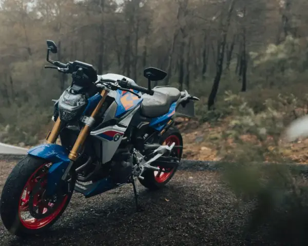 Niebiesko-biały motocykl BMW F900R z czerwonymi felgami na tle jesiennego lasu.