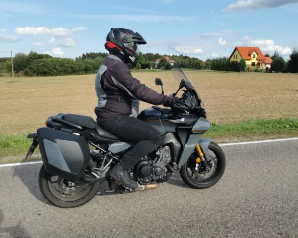Motocyklista na Yamaha Tracer 900, z sakwami, w kasku, jedzie po drodze. Dane techniczne tego modelu są imponujące.