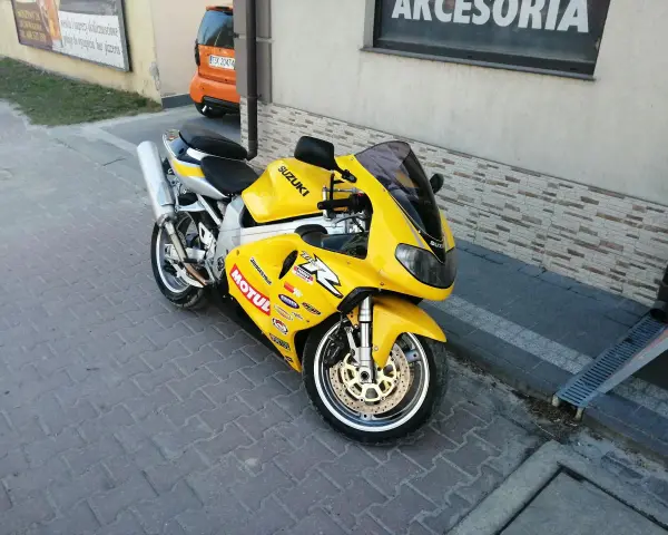 Żółty motocykl Suzuki TL1000R z naklejkami sponsorów, zaparkowany na chodniku.