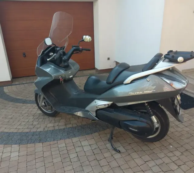 Szary skuter Honda Silver Wing 600 stoi na kostce brukowej przed garażem.