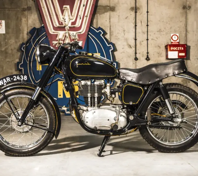 Czarny motocykl Junak, który produkuje polska fabryka, z żółtymi wstawkami i tablicą rejestracyjną WAR-2438.